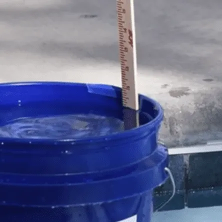 Ruler measuring pool-water loss on the outside of a bucket during a pool bucket test