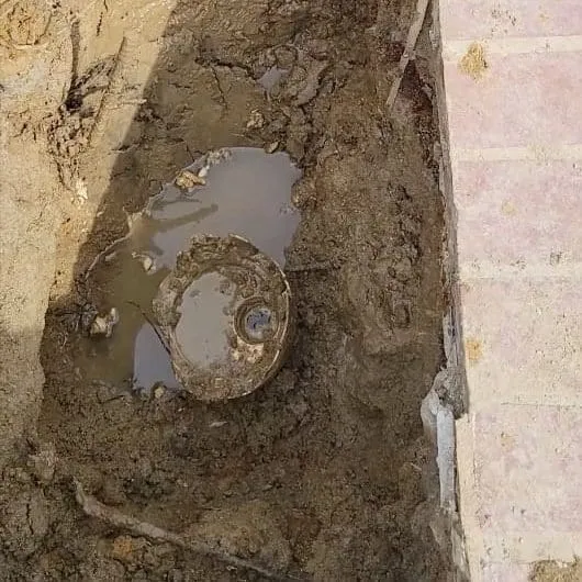 Muddy excavation beside a swimming pool during a leak repair